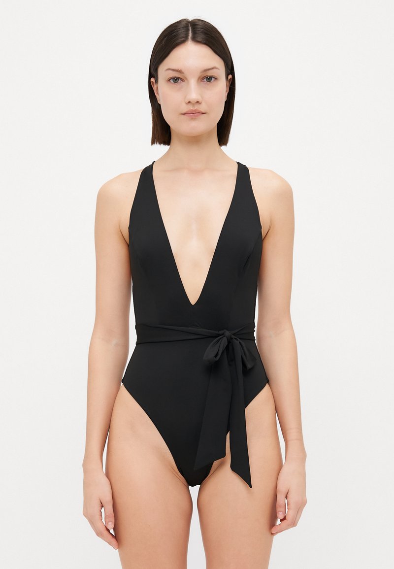 Black one-piece swimsuit featuring a deep V-neck, wide straps, and a tied accent at the waist, made from smooth, stretchy fabric.
