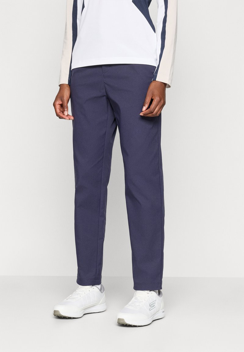 Navyblaue Hose mit geradem Schnitt, aus glattem Stoff gefertigt, kombiniert mit weißen Sportschuhen mit strukturiertem Obermaterial.