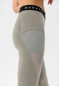 Høyt midjebelte leggings i lysegrå med mesh og teksturerte detaljer. Elastisk midjebånd med "MOROTAI"-merke. Distinkte geometriske utskjæringer.