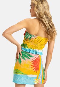 Conjunto de dos piezas colorido, que presenta una blusa amarilla con fruncidos y una falda corta con un vibrante estampado tropical de sol, palmeras y olas del océano.