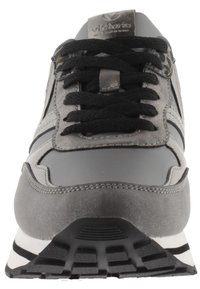 Zapatilla gris con una textura de cuero liso y ante, cordones negros y suela a rayas blanca y negra. Presenta un acabado metálico y patrones sutiles.