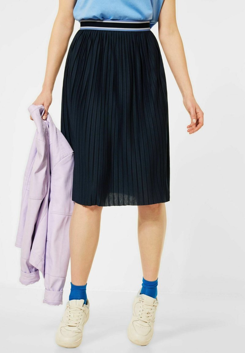 Černá plisovaná midi sukně s elastickým pasem, ozdobená bílo-námořnickým pruhem. V kombinaci s lehkým fialovým sáčkem a bílými teniskami.