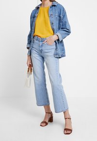 Jeansowa kurtka, żółty top, jasnoniebieskie dżinsy z postrzępionym dołem, brązowe sandały na słupku oraz biała torebka z koralikowym uchwytem.