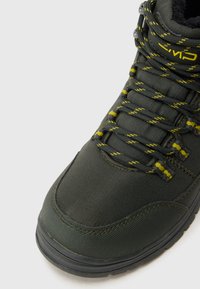 Vihreä tekstiilinen vaelluskenkä, jossa on karkeapintainen viimeistely, kelta-mustakuviolliset nauhat, pehmustettu kaulus ja kumipohja.