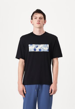 Schwarzes Baumwoll-T-Shirt mit kurzen Ärmeln, das ein rechteckiges blau-weißes Muster über der Brust zeigt.