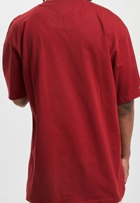 Rotes Baumwoll-T-Shirt mit kurzen Ärmeln, Rundhalsausschnitt und lockerer Passform. Zeigt minimale Nahtdetails und eine glatteTextur.