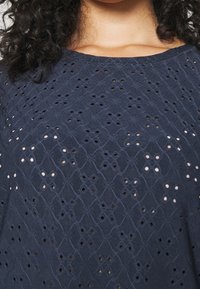 Navy blue top featuring intricate diamond and circular cut-out patterns, with a soft texture and round neckline.