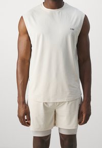 Completo sportivo color crema composto da canotta e pantaloni corti. La canotta presenta un collo rotondo e un design senza maniche, mentre i pantaloni corti hanno uno strato interno aderente.