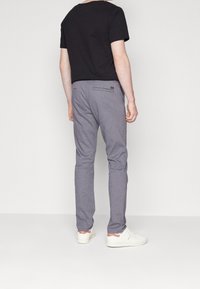 Pánské šedé kostkované kalhoty s úzkým střihem, vybavené dvěma zadními kapsami a jemným texturovaným vzorem, zkombinované s černým tričkem a bílými teniskami.