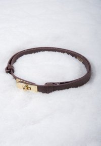 Brown leather belt with gold buckle, featuring a smooth texture and adjustable length, laid on a snowy surface.