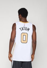 Witte basketbalshirt met zwarte en gouden accenten. Bevat de naam "TATUM" en het nummer "0" op de achterkant, met een logo bij de halslijn.