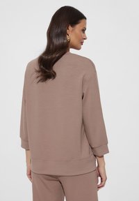 Brązowy, oversize'owy sweter z miękkiej tkaniny, o rękawach do trzech czwarte, z prostym, nieozdobionym wzorem i ściągaczem u dołu.