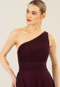 Asymmetrisches burgunderfarbenes Kleid mit strukturierten Falten, tailliertem Schnitt und fließendem Rock. Hergestellt aus glattem Stoff, mit einem Schulterträger.