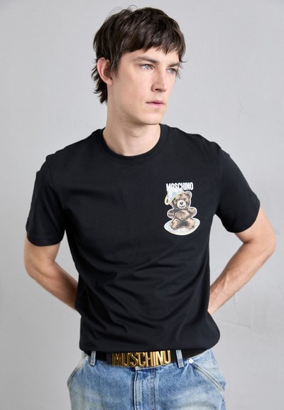 Svart bomull T-skjorte med et bjørnegrafikk på venstre bryst, kombinert med denimjeans og et gull Moschino-logo belte.