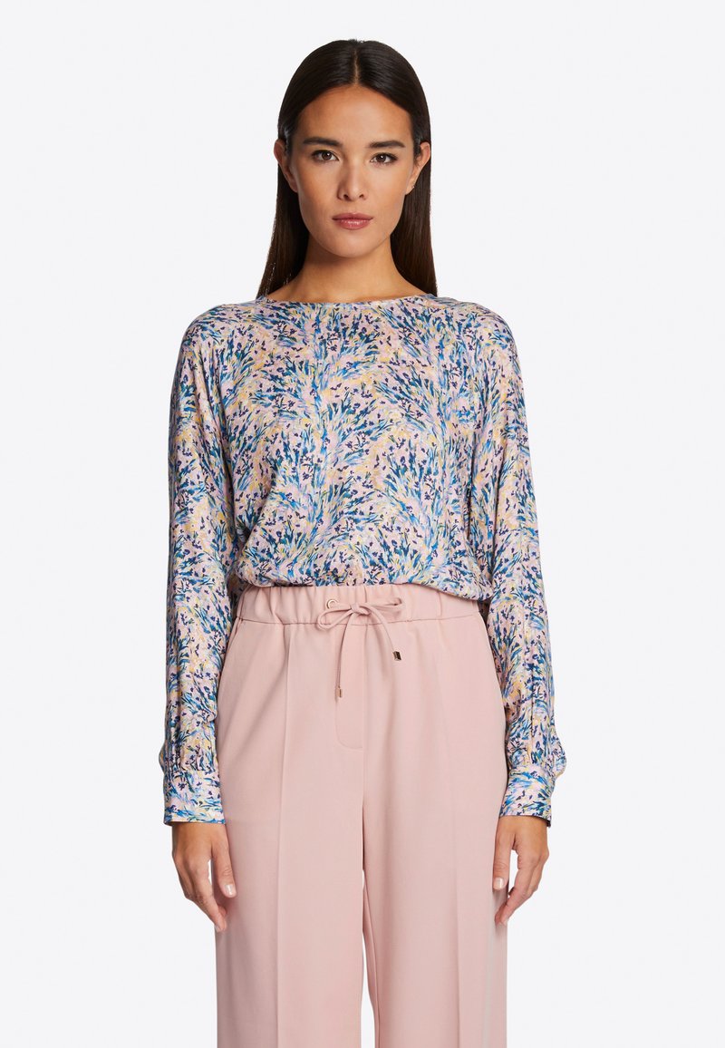 Langärmlige Bluse in Hellrosa mit floralem Muster in Blau und Grün. Weicher Stoff mit lässiger Passform, kombiniert mit hochgeschnittenen, hellrosa Hosen.