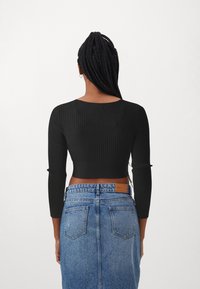 Schwarzes, geripptes Crop-Top mit langen Ärmeln, kombiniert mit einem hochgeschnittenen blauen Denim-Rock, der ein Lederlabel und Gesäßtaschen aufweist.