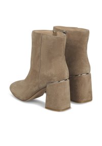 Bottines en daim beige avec un talon bloc géométrique et des détails argentés. Fermeture éclair à l'arrière. Texture lisse et bout arrondi.