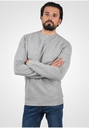 Light gray ribbed sweater with long sleeves, round neckline, and textured design. Worn with blue jeans against a neutral background.
