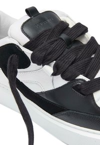 Białe i czarne sneakersy wykonane z gładkiej skóry i zamszu, z grubymi czarnymi sznurówkami oraz wyściełanym kołnierzem wokół kostki z logo.