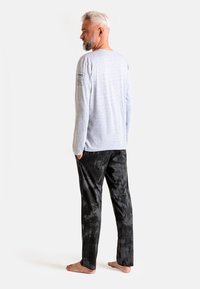 Szara koszula z długim rękawem z logo na lewym rękawie, w zestawie z czarnymi spodniami w tie-dye, wykonana z bawełnianego materiału, o luźnym kroju, noszona na boso.