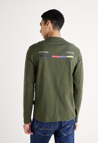 Olīvzaļš krekls ar garām piedurknēm, kas aizmugurē rotāts ar "Pepe Jeans" un "Red Bull Racing" logo, kā arī krāsainu horizontālu svītru detaļu.