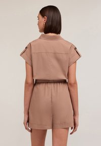Giocoso corto color nocciola con colletto, maniche arrotolate, vita arricciata e tessuto liscio con una vestibilità rilassata.
