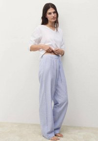 Camicia bianca a maniche lunghe abbinata a pantaloni da pigiama a strisce blu chiaro e bianche con cintura elastica e dettaglio con lacci.