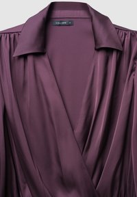 Blusa bordeaux con colletto, featuring maniche plissettate e design avvolgente. Realizzata in tessuto liscio e leggero con un leggero luccichio.