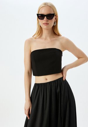 Top corto negro sin tirantes hecho de material suave, con un diseño simple y una cremallera lateral. Combinado con una falda negra fluida.