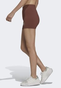 Hnedé vysoké šortky s hladkou textúrou a detailom loga. Skombinované s bielymi športovými topánkami so sivými akcentmi a textúrovanou podrážkou.