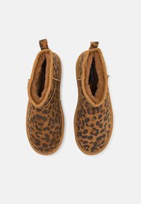 Hnědé kotníkové boty s leopardím vzorem, s měkkým a nadýchaným vnitřním polstrováním. Vyznačují se krátkým, zaobleným designem a poutkem na patě.