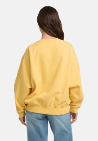 Sweatshirt jaune surdimensionné avec un col rond, des poignets et un ourlet côtelés ; en tissu coton, coupe décontractée ; détails de couture visibles.