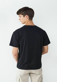 Czarna koszulka bawełniana z okrągłym dekoltem i krótkimi rękawami. Tył ma gładką teksturę bez widocznych grafik lub wzorów.