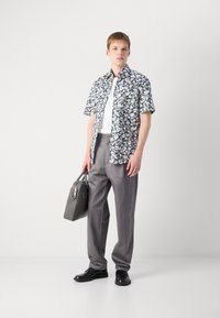Kortermet blomstret skjorte i hvit, blå og grønn; grå dressbukser; svarte sko; grå håndveske med sølvfarget detaljer.