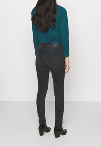 Jeans skinny negros de cintura alta, hechos de mezclilla, con un ligero desgastado, dos bolsillos traseros y una cinturilla lisa. Combinados con una blusa azul verdosa.