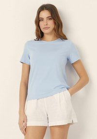 Camiseta de manga corta azul claro en tela suave con un corte relajado y escote redondo, combinada con pantalones cortos de lino blancos. Diseño sencillo y clásico.