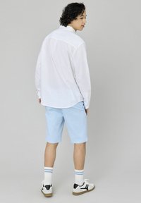 Chemise blanche à manches longues, shorts bleu clair, chaussettes blanches avec des rayures bleues et baskets noir et blanc, vues de dos.