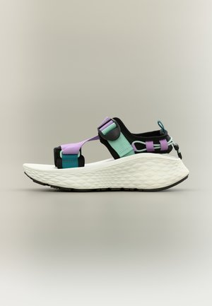 Sandale multicolore avec une semelle blanche texturée, des brides ajustables bleu sarcelle, lavande et noir, et une boucle arrière pour un enfilage facile.