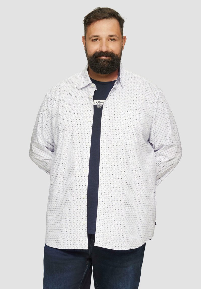 Chemise blanche à boutons avec de petits pois bleus et jaunes, à manches longues et à coupe décontractée, portée par-dessus un T-shirt noir. Jean en denim.