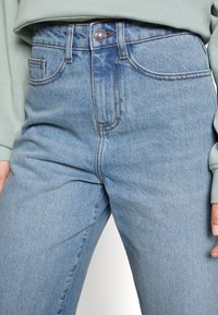 Ljusblå jeans i denim med skräddarsydd passform, hög midja, fem fickor och kontrasterande orange sömnad på sömmarna.