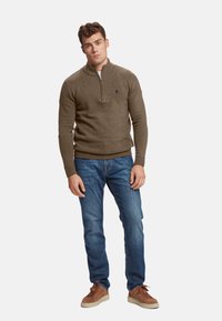 Pulover maro cu guler cu jumătate de fermoar, asortat cu blugi albaștri și adidași din suede maro. Puloverul are o textură subtilă și un logo.
