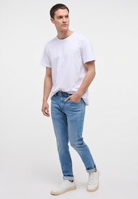 Valge puuvillane T-särk, helesinised teksad ja valged sneakers. T-särgil on peen logo; teksad on klassikalise lõikega. Sujuv ja juhuslik stiil.