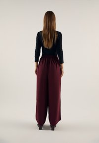 Pantalon large bordeaux avec taille élastique associé à un haut noir à manches longues. Texture lisse, coupe décontractée et longueur cheville.