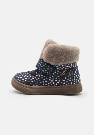 Botte d'enfant bleu foncé avec des pois irisés, semelle marron, fermeture à scratch et doublure beige en peluche au niveau du revers.