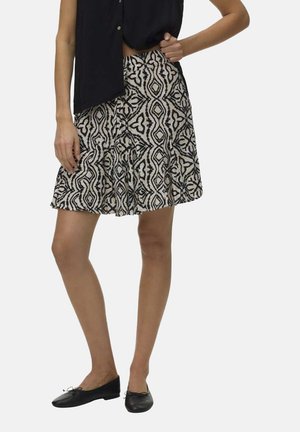 Femme portant un haut noir sans manches et une jupe mi-longue à motif géométrique abstrait noir et blanc, assortis à des ballerines noires.