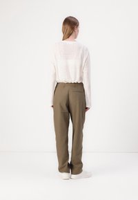 Chemise légère crème à manches longues avec une coupe décontractée, associée à un pantalon vert olive muni d'une poche arrière et de jambes fuselées.