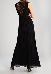 Svart maxiklänning med korta ärmar, spetsdetalj på ryggen och fransad midja. Flödande silhuett, mjukt tyg och genomskinligt kjoldel.