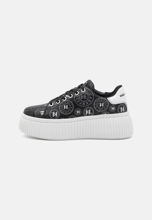 Zapatilla de plataforma negra con patrones circulares blancos de logotipo, cordones negros, suela blanca gruesa acanalada y lengüeta trasera blanca con la etiqueta "KARL LAGERFELD."