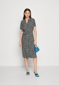 Svart blommig klänning med korta ärmar, figursydd midja, knälång kjol, kombinerad med blå handväska och teal öppna tåskor.