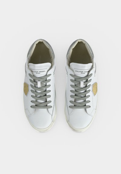 Ζευγάρι λευκά δερμάτινα sneakers με γκρι κορδόνια, γκρι λεπτομέρεια στη φτέρνα και χρυσή πινελιά στις εξωτερικές πλευρές, από πάνω.